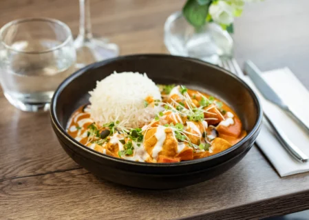 Delicious curry and rice in elegant hotel dining, garnished with microgreens, next to glass of water and cutlery.