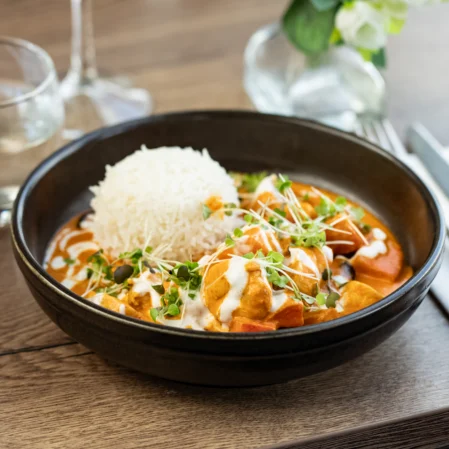 Delicious curry and rice in elegant hotel dining, garnished with microgreens, next to glass of water and cutlery.