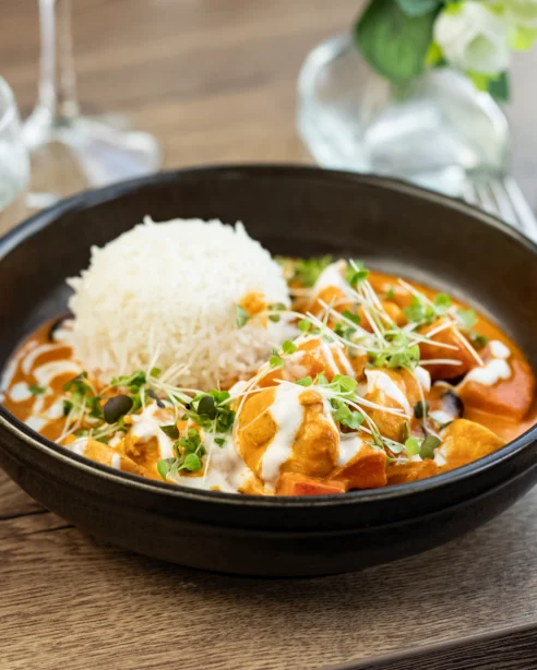 Delicious curry and rice in elegant hotel dining, garnished with microgreens, next to glass of water and cutlery.