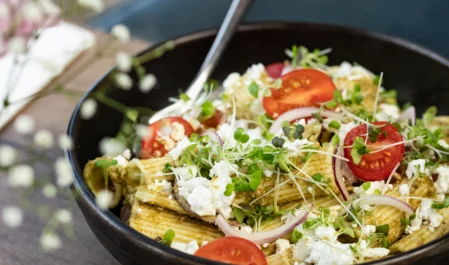Delicious pasta salad with fresh tomatoes and microgreens on a wooden table at a welcoming hotel restaurant.