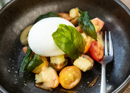 Fresh burrata salad with ripe cherry tomatoes and basil, served beautifully on a wooden table at our hotel restaurant.
