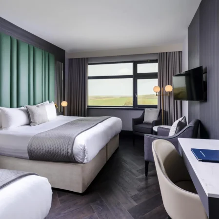 Stylish hotel room with king-size bed, scenic window view, modern decor, desk, seating area, and flat-screen TV.
