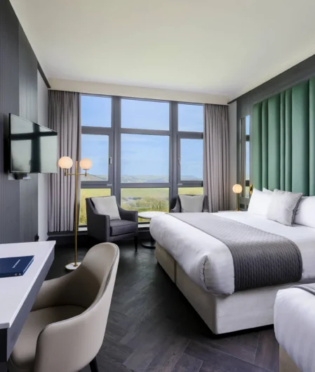 Spacious hotel room with double beds, ocean view, modern decor, desk area, seating, TV, and elegant lighting.