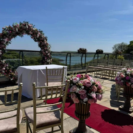 Elegant outdoor wedding venue with floral arch, scenic water view, and decorated seating arrangement at luxury hotel.