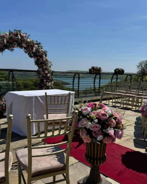 Elegant outdoor wedding venue with floral arch, scenic water view, and decorated seating arrangement at luxury hotel.