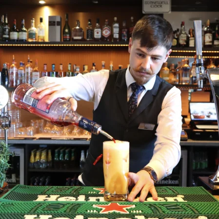 Bartender pouring cocktail at stylish hotel bar with various spirits and modern decor.