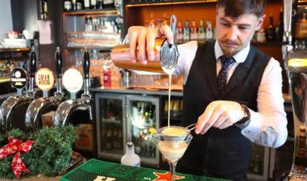 Bartender crafting cocktail at stylish hotel bar, featuring premium drinks and festive decor.