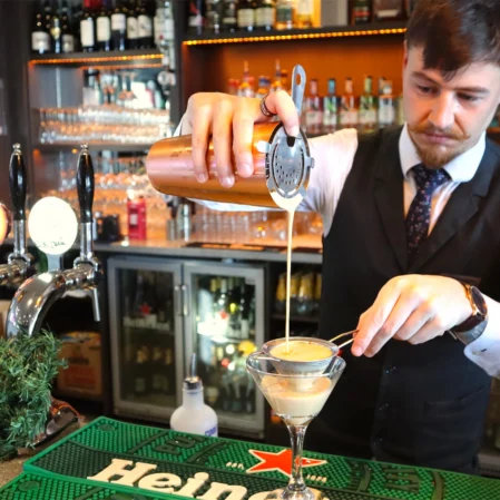 Bartender crafting cocktail at stylish hotel bar, featuring premium drinks and festive decor.