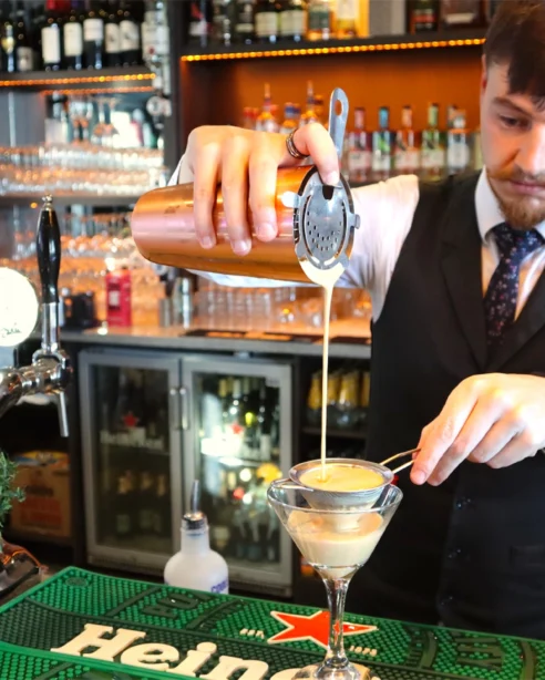 Bartender crafting cocktail at stylish hotel bar, featuring premium drinks and festive decor.