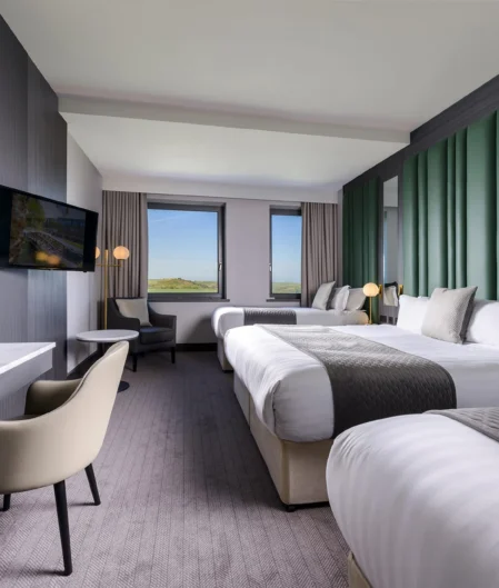 Spacious, modern hotel room with twin beds, plush seating, desk, wall-mounted TV, and scenic countryside views.