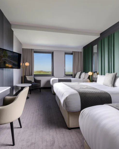 Spacious hotel room with two double beds, modern decor, scenic countryside view, desk, and flat-screen TV for a relaxing stay.