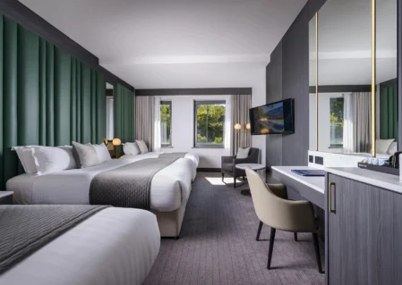 Modern hotel room with two beds, elegant decor, large windows, natural light, desk, and flat-screen TV for a cosy stay.