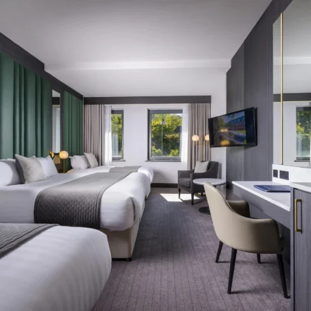 Modern hotel room with two beds, elegant decor, large windows, natural light, desk, and flat-screen TV for a cosy stay.