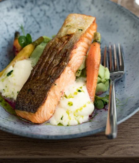Tasty grilled salmon with fresh vegetables and creamy mashed potatoes served on a charming wooden table in hotel dining.