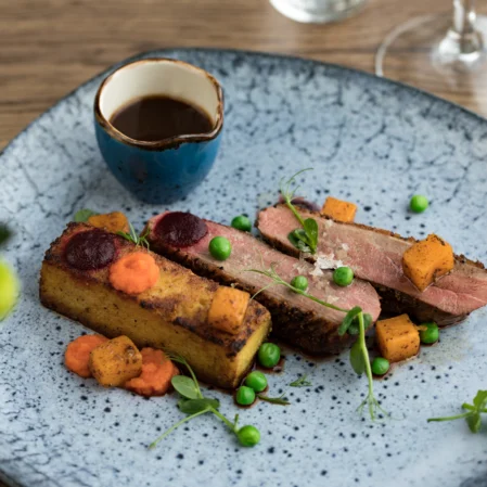 Gourmet duck breast with roasted vegetables and gravy, elegantly plated for fine dining experience at luxury hotel.
