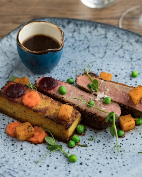 Gourmet duck breast with roasted vegetables and gravy, elegantly plated for fine dining experience at luxury hotel.