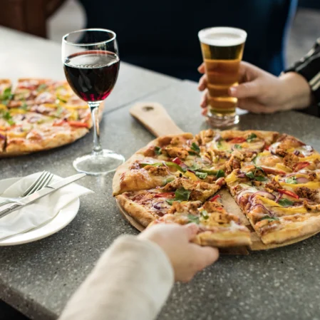 Guests enjoying gourmet pizza with wine and craft beer at a stylish hotel restaurant table.
