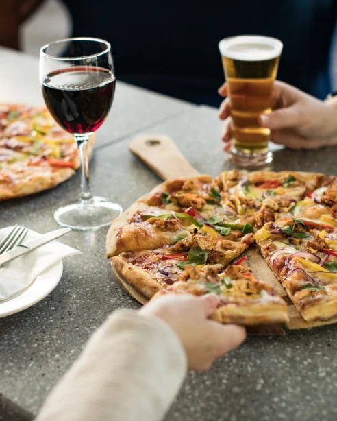 Guests enjoying gourmet pizza with wine and craft beer at a stylish hotel restaurant table.