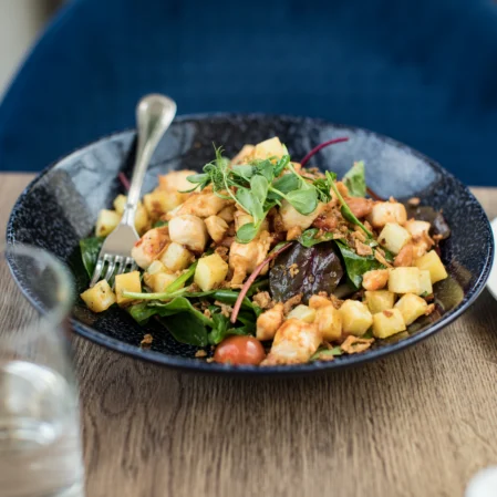 Gourmet chicken salad with fresh greens, cherry tomatoes, and crispy potatoes on a wooden table in a stylish hotel restaurant.