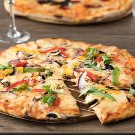 Gourmet pizza with fresh toppings on a wooden table, paired with red wine, inviting dining experience.