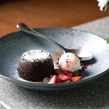 Elegant dessert with chocolate fondant, fresh strawberries, and vanilla ice cream on a granite table in luxury hotel restaurant.
