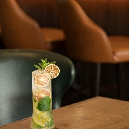 Refreshing mojito on wooden table at chic hotel bar with stylish leather chairs in background, perfect for relaxing.