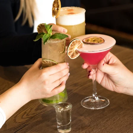 Guests enjoying vibrant cocktails at stylish hotel bar, featuring fresh garnishes and cosy ambience for relaxation.
