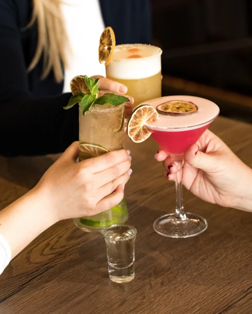Guests enjoying vibrant cocktails at stylish hotel bar, featuring fresh garnishes and cosy ambience for relaxation.