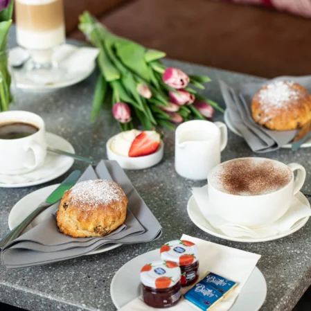 Cosy café breakfast spread with pastries, coffee, and tulips on a granite table, creating a welcoming atmosphere.