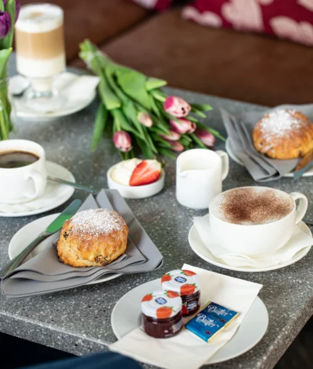 Cosy café breakfast spread with pastries, coffee, and tulips on a granite table, creating a welcoming atmosphere.