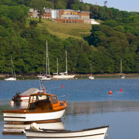 Scenic hotel on a lush hillside overlooking a tranquil bay with moored sailboats, promising peaceful retreats and nature views.