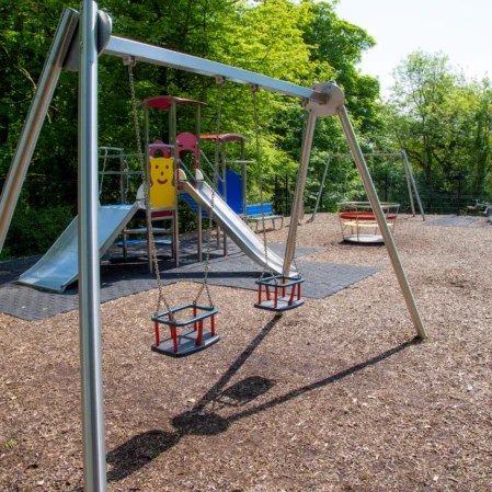 Spacious hotel playground with swings, slides, and climbing frames surrounded by lush greenery, perfect for family fun.