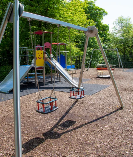 Spacious hotel playground with swings, slides, and climbing frames surrounded by lush greenery, perfect for family fun.