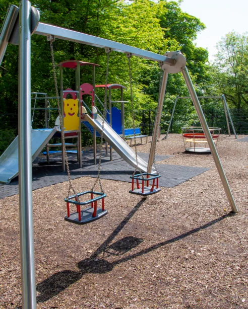 Spacious hotel playground with swings, slides, and climbing frames surrounded by lush greenery, perfect for family fun.