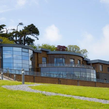 Modern hotel with glass facade, lush green lawn, and scenic views, offering a peaceful retreat and luxury amenities.