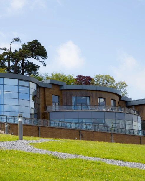 Modern hotel with glass facade, lush green lawn, and scenic views, offering a peaceful retreat and luxury amenities.