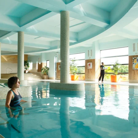 Luxurious indoor pool with skylights, elegant columns, and tropical plants; a tranquil spa retreat experience.