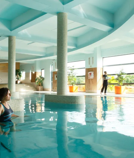 Luxurious indoor pool with skylights, elegant columns, and tropical plants; a tranquil spa retreat experience.