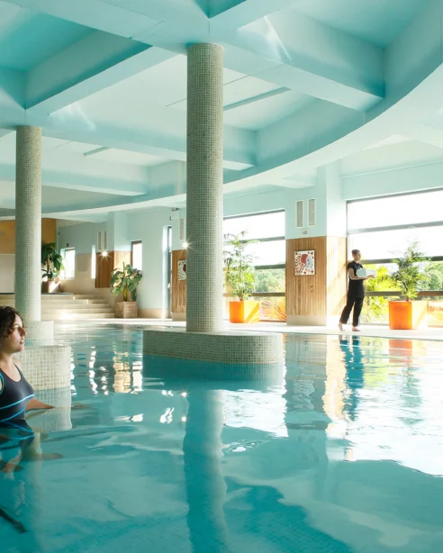 Luxurious indoor pool with skylights, elegant columns, and tropical plants; a tranquil spa retreat experience.