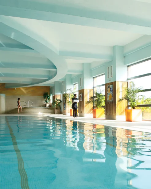 Luxurious indoor pool with natural light, elegant decor, and modern amenities for a relaxing hotel experience.