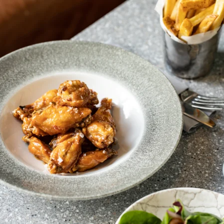 Crispy chicken wings and golden chips at hotel restaurant, alongside fresh salad and a crisp pint of beer on a stone table.