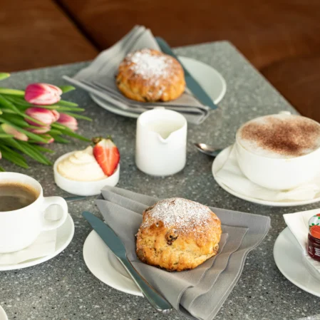 Delicious afternoon tea with scones, coffee, and tulips on a stone table at a welcoming hotel lounge.