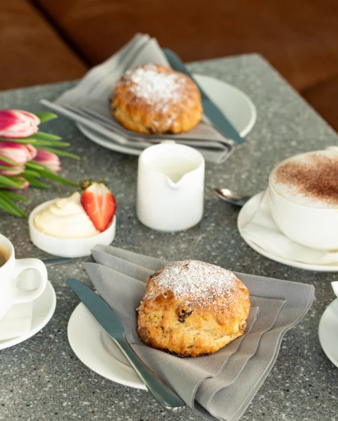 Delicious afternoon tea with scones, coffee, and tulips on a stone table at a welcoming hotel lounge.