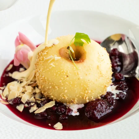 Elegant dessert with custard, berry sauce, and almonds, served on a white plate, promising a gourmet hotel dining experience.