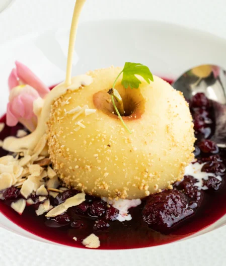 Elegant dessert with custard, berry sauce, and almonds, served on a white plate, promising a gourmet hotel dining experience.