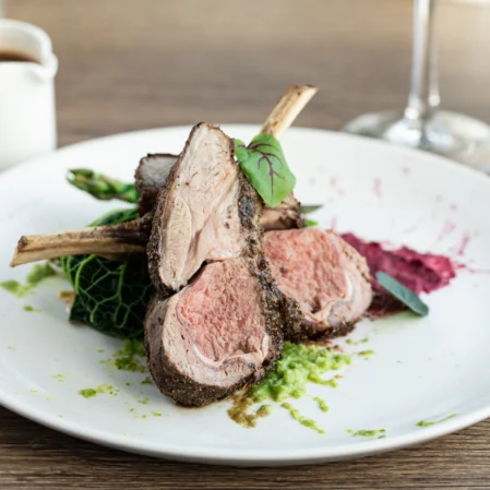 Delicious herb-crusted lamb on a white plate with vibrant greens and beet puree, highlighting gourmet dining experience.