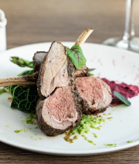 Delicious herb-crusted lamb on a white plate with vibrant greens and beet puree, highlighting gourmet dining experience.