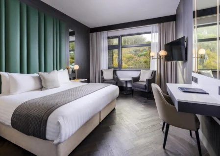 Modern hotel room with king-size bed, stylish decor, large window view, comfy seating, and workspace. Ideal for relaxation.
