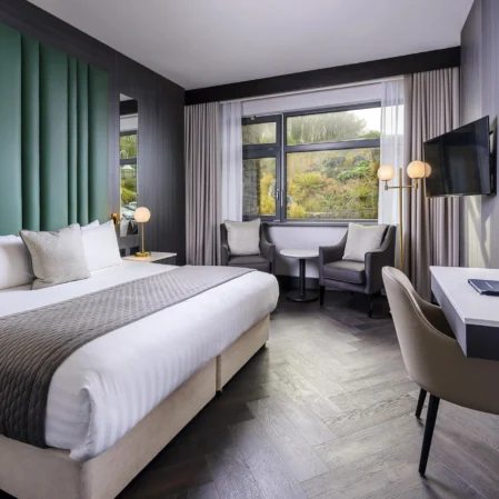 Modern hotel room with king-size bed, stylish decor, large window view, comfy seating, and workspace. Ideal for relaxation.