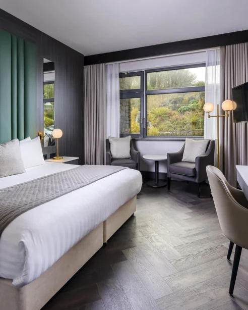 Modern hotel room with king-size bed, stylish decor, large window view, comfy seating, and workspace. Ideal for relaxation.